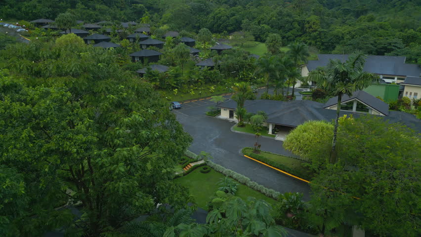 Backwards fly above dense lush green trees and vegetation around accommodation facility. Tilt up reveal low clouds above vast forest. La Fortuna, Costa Rica