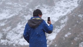 Slow motion shot of an Indian man shooting video of the snowfall with his mobile phone during the winter season at Sissu in Himachal Pradesh, India. Man taking video of snowfall for his social media.