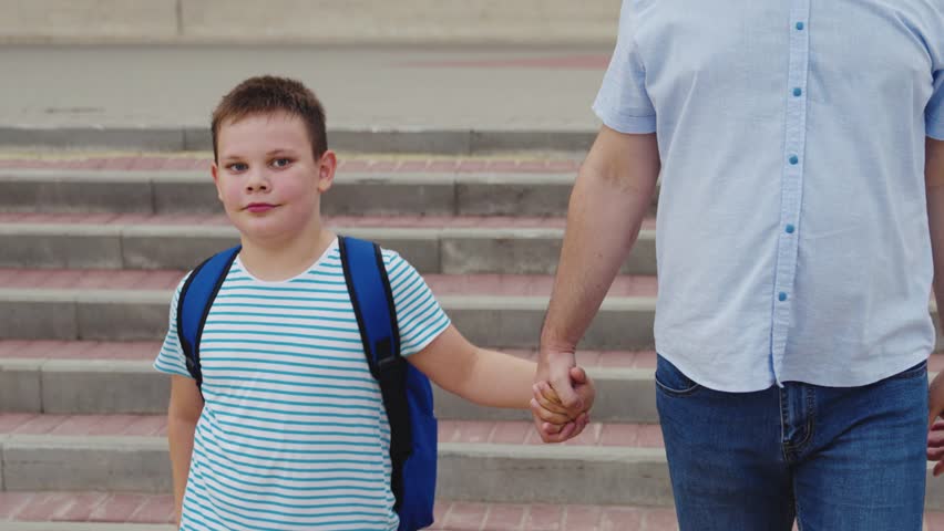 boy son holding his father hand crosses road through pedestrian crossing. happy family concept. dad helps child boy cross road school lesson. zebra road. first grader with school bag back. happy boy.
