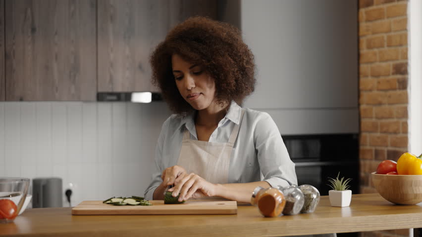 Smiling woman slicing cucumber in the kitchen, cooking vegetarian dinner | Shutterstock HD Video #1100254775