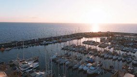 Luxury yachts docked by the golden coast of Spain during magical sunset lights. Luxury holiday concept. Aerial video of luxury super yacht marina and sailing boats.