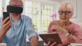 Retired senior couple at home in kitchen using variety of modern tech including VR headset,digital tablet, mobile phone and smart watch - shot in slow motion - Powered by Shutterstock - Get 15% off with code: PIKWIZARD15