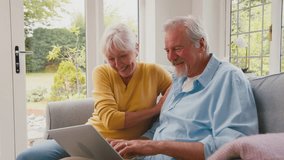 Excited retired senior couple with laptop sitting on sofa in lounge shopping online or booking holiday - shot in slow motion - Powered by Shutterstock - Get 15% off with code: PIKWIZARD15