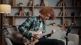 Red-haired curly-haired man sits on the sofa and plays the guitar - Powered by Shutterstock - Get 15% off with code: PIKWIZARD15