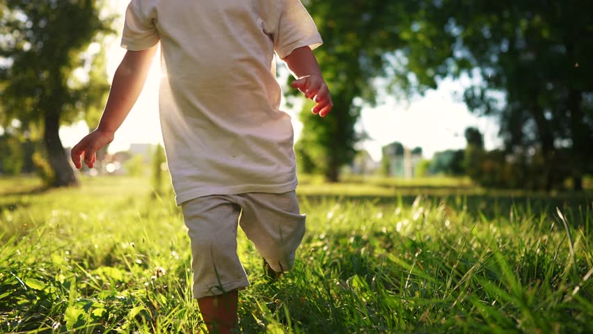 Bare feet. baby boy is playing in the forest park. close-up child legs run on the park green grass in the park. family childhood dream concept. a child in sneakers run on the grass in a fun park | Shutterstock HD Video #1100260923