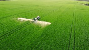 Aerial video of tractor spraying soil and young crop in springtime in field. Tractor spraying pesticides on soy field with sprayer at spring. Nozzle of the tractor sprinklers sprayed.