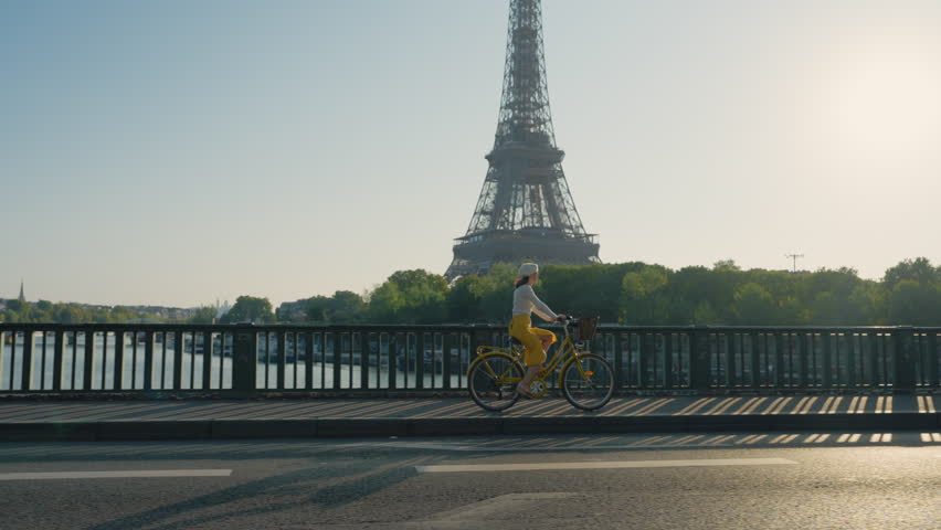 Happy girl riding a yellow bicycle on a bridge overlooking the Eiffel Tower