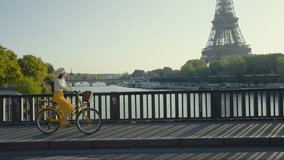 Attractive Parisian woman riding a yellow bicycle on a bridge overlooking the Eiffel Tower