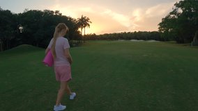 A stunning slow-motion stock video captures a beautiful moment of motherhood. A pregnant woman, dressed in a pink t-shirt and shorts, walks gracefully through a lush green field with a yoga mat in