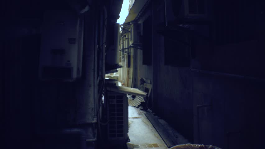 walking view of ghetto old dirty asia building in dark narrow fire escape back alley with electricity poles and cables hanging across in sky and all bared window balcony and aircon machine hanging  