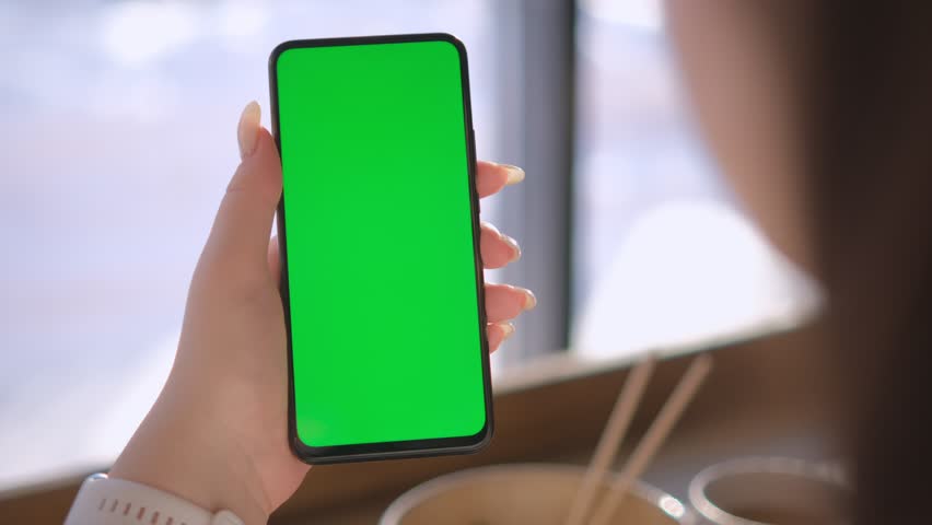 Woman Hand. Cup of Hot coffee and Using Smartphone Watching Green Screen Top View. Smartphone with Green Mock-up Screen Business Concept. Woman is Holding Smartphone with Green Screen in cafe | Shutterstock HD Video #1100266685