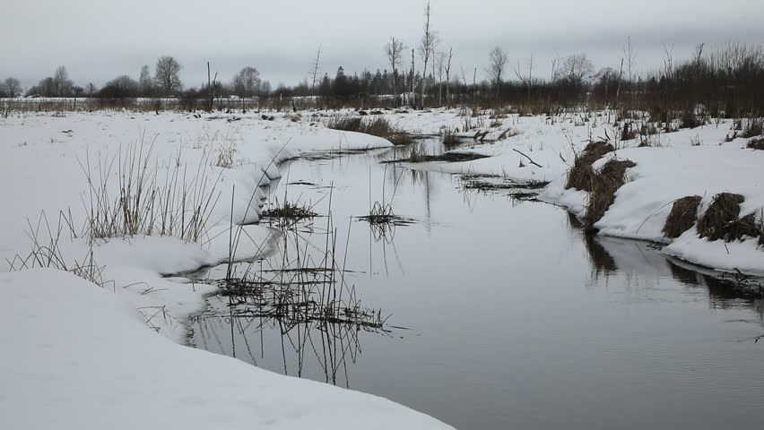 Winter landscape with an unfrozen river in the distance forest.