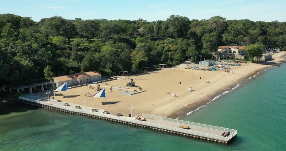 Large suburban public beach in Glencoe, Illinois with long pier along the Lake Michigan shoreline with sailboats and kayaks.
