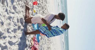 Vertical video of happy african american mother and son on beach having fun together. Holidays, vacations and spending quality family time together concept.