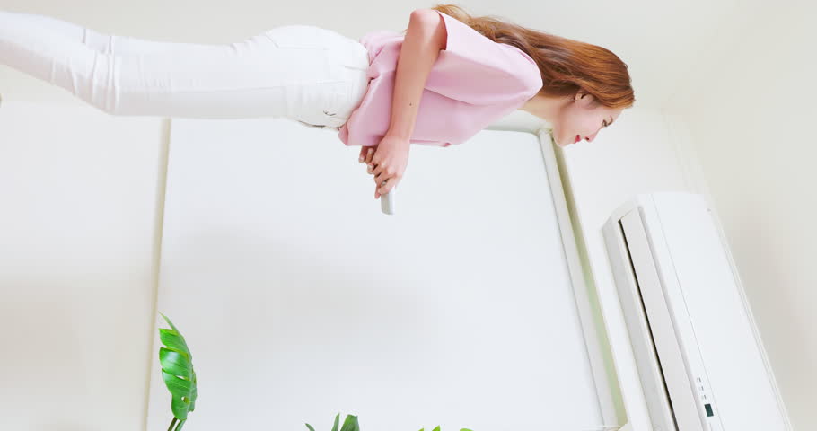 vertical of asian woman is turning on air conditioner through switching remote controller at home