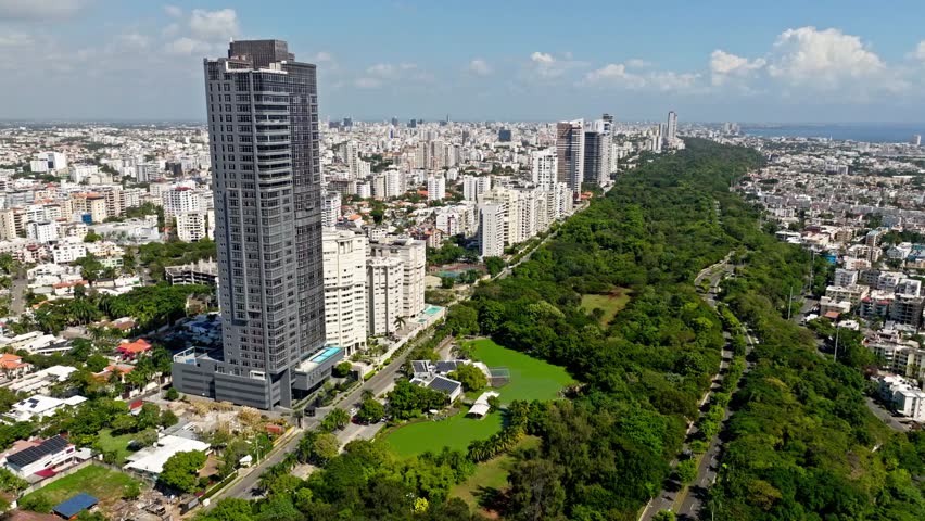 Drone flying near new and modern skyscraper in Avenida Anacaona with panoramic view of Santo Domingo city, Dominican Republic. Aerial forward