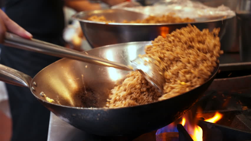 Chef flips fried rice in wok over flaming fire on commercial stovetop in restaurant kitchen, slow motion close up 4K Royalty-Free Stock Footage #1100284977