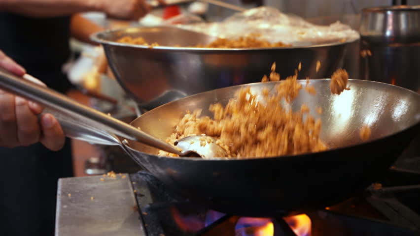 Chef flips and tosses fried rice in wok over flaming fire on commercial stovetop in restaurant kitchen, slow motion close up 4K