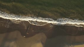 Slow-motion of isolated and unrecognizable person running along beach with dog at sunset. Aerial top-down sideways directly above
