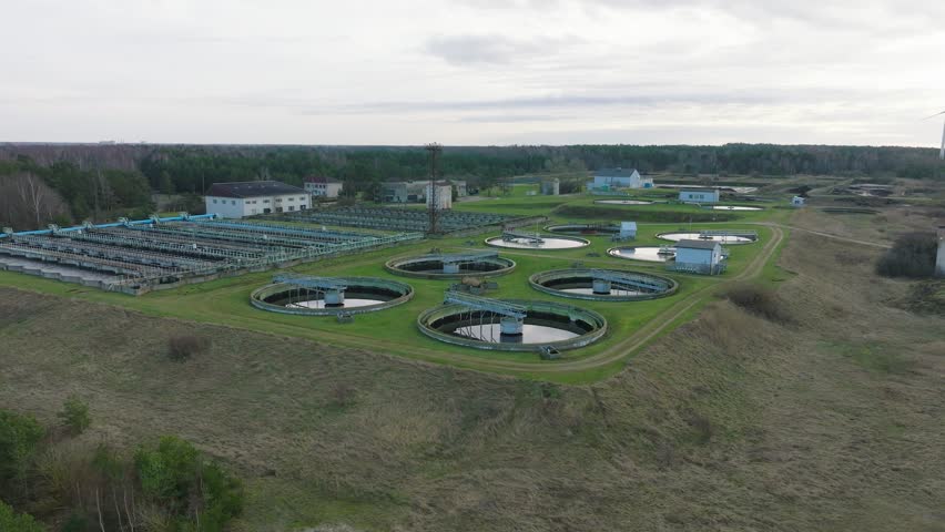 Aerial establishing view of water basins at sewage treatment plant, ponds for recycling dirty wastewater, recycle system technology, waste management theme, wide drone shot moving forward | Shutterstock HD Video #1100285381