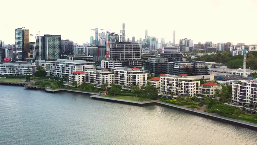 Aerial view fly around the river capturing Newstead river terrace, waterfront residential apartment complex with downtown cityscape on the skyline at sunset, Brisbane, capital city of Queensland.