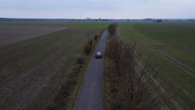 The car is driving on the road in the field. Flying over the car. Video from a drone. Green meadow. The car makes a figure of eight. The car goes like in the movies. Summer landscape