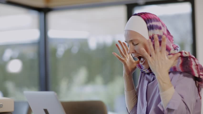 Female in hijab is sitting at the table in front of a laptop | Shutterstock HD Video #1100294141