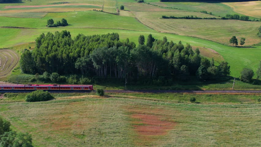 Red Train on Railroad. Passenger Train Aerial View of Public Transport Infrastructure in Poland Landscape. Passenger Electric Train Passing Through Farm Fields In Beautiful European Countryside. Royalty-Free Stock Footage #1100294361
