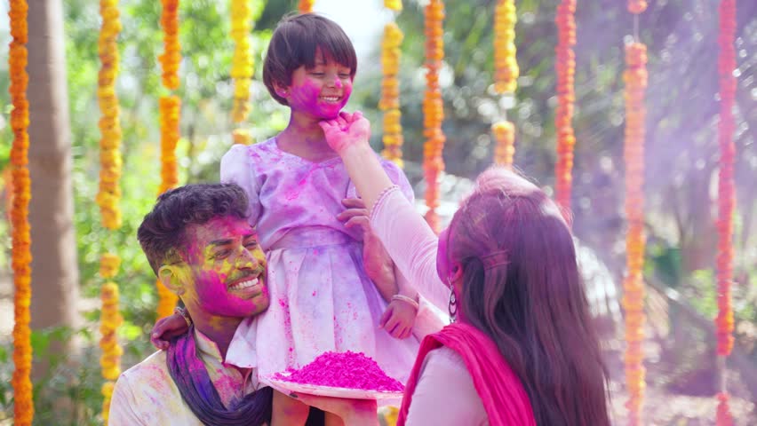 Young mother applying holi colors to daughter while kid on father shoulder - concept of holi festival celebration, parenthood and relationship bonding Royalty-Free Stock Footage #1100301995