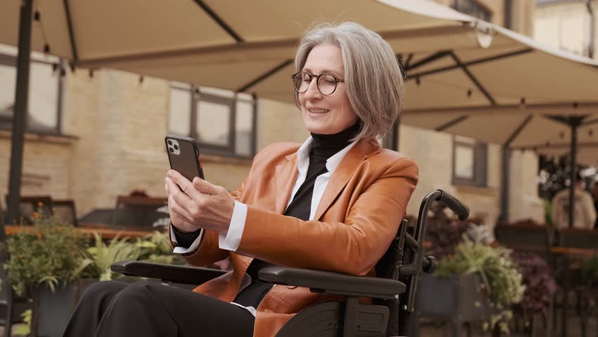 Elderly woman in a wheelchair on the street talking on the phone and smiling