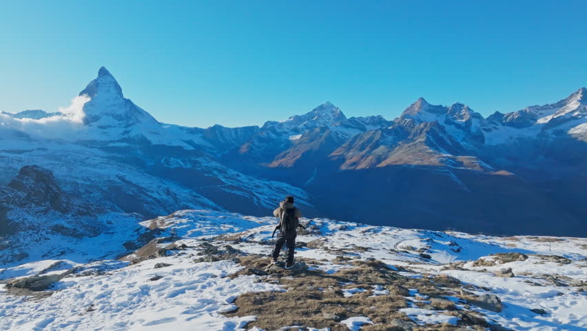 Young man backpacker take a photo by camera at Switzerland mountain peak view point with iconic famous landscape Matterhorn background. Aerial drone orbit shot, Nature, Travel and Adventure concept.