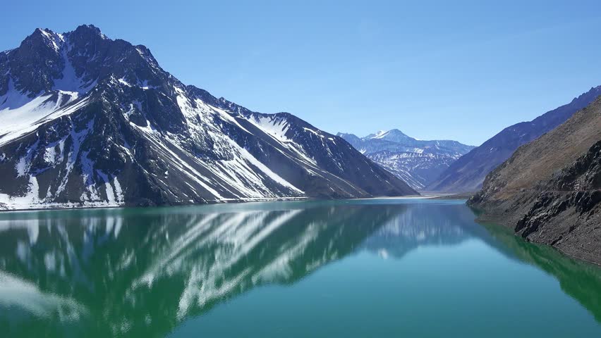 A picturesque lake surrounded by snow-capped mountains. Santiago, Chile, Andes. Travel. Reflection of mountains in a lake with clear water