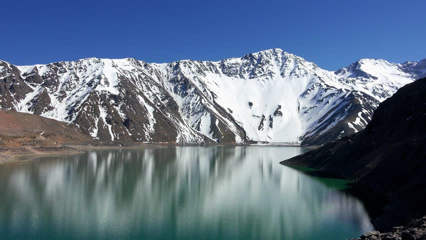 A picturesque lake surrounded by snow-capped mountains. Santiago, Chile, Andes. Travel. Reflection of mountains in a lake with clear water