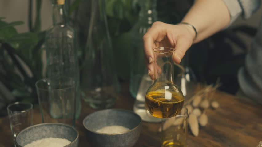 Handmade. Apprentice. Cosmetics made from natural herbs. Preparation of oil from the harvest. Wooden table and old flasks. Mystery. Recipes for youth. Natural olive oil. Royalty-Free Stock Footage #1100312161