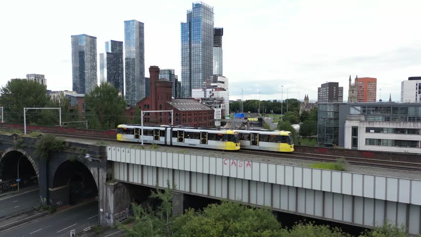 Aerial drone flight alongside a tram on a bridge showing a background of Manchester City Centre skyscrapers and apartment buildings Royalty-Free Stock Footage #1100312377