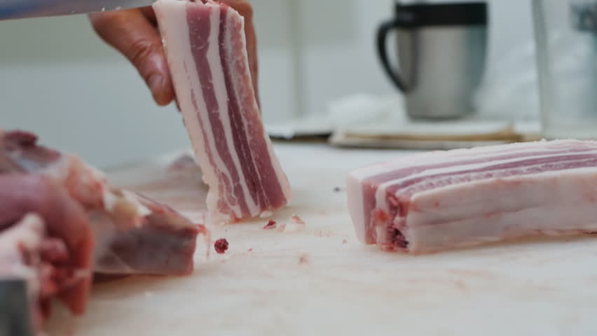 Close-up of cutting raw fatty meat with layers of fat on a cutting board with a sharp knife. Butcher's hands holding a knife cut pieces of meat for trade in a butcher's shop Royalty-Free Stock Footage #1100316011