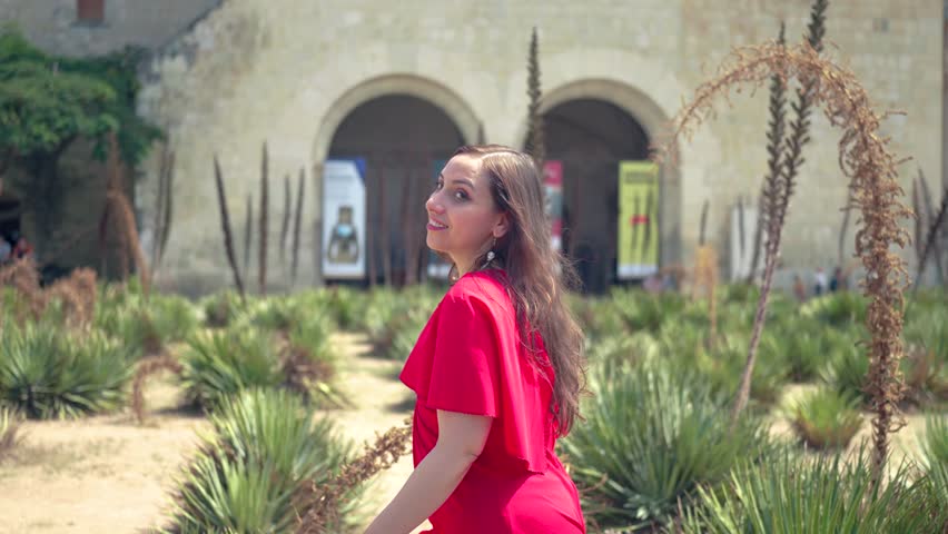 Slow motion of woman walking near Church of Santo Domingo de Guzmán, happy Hispanic female in red dress looking and spinning around while strolling on sunny day in center of Oaxaca, Mexico