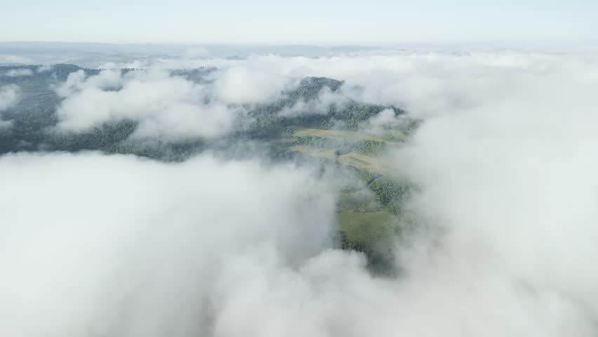 Flying above the clouds over beautiful forest, mountain and river below. Aerial. Drone. 4K. Hole in the clouds.