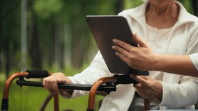 Nurse helping elderly woman to make a video call on tablet in park, mobile app
