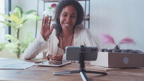 Young happy African American woman coach conducts video broadcast for visitors in social networks or subscribers to support psychological state of employees sits at table with tablet