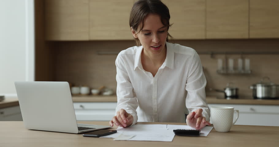 Focused young homeowner woman using calculator, laptop, checking paper bills, receipts, counting domestic budget, finding profit, getting cheerful, happy, doing home paperwork at kitchen table Royalty-Free Stock Footage #1100336973