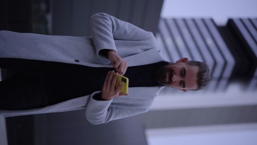 Vertical video of handsome young businessman checks his next meeting on the cell phone outside a business center. Close up portrait of manager thumb up smiling to camera outdoors. Enterprising people.