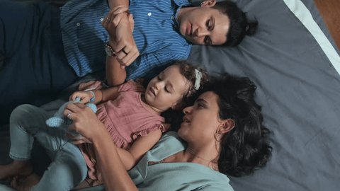 Top view of happy Caucasian lesbian couple and their beloved little daughter playing while lying on bed at home together – Video có sẵn
