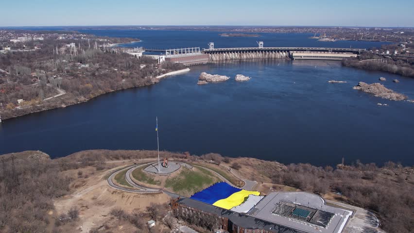 People hold a large flag of Ukraine. Dam, aerial view of the Dnieper hydroelectric station. Khortytsya Island, Zaporozhye, Ukraine.