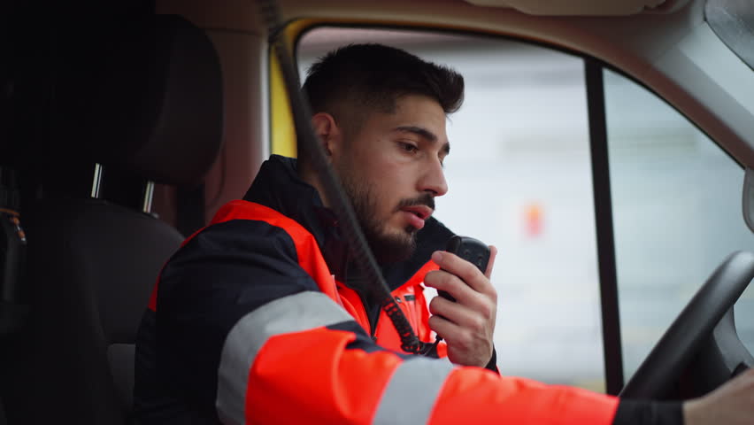 Young man doctor sitting and talking in to walkie-talkie in ambulance car. Royalty-Free Stock Footage #1100340387