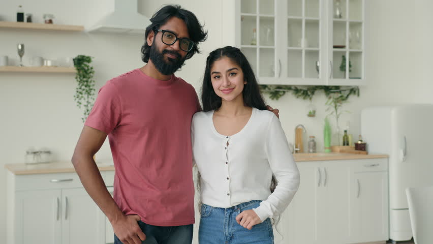 Portrait of two people multiracial couple in love posing in domestic white kitchen. Arabian hispanic indian ethnic family partners married woman and man spouses homeowners hugging at home apartment Royalty-Free Stock Footage #1100340727