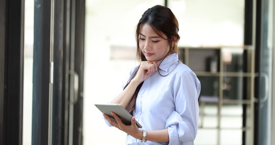 Asian businesswoman working with digital tablet standing at office workplace. | Shutterstock HD Video #1100343315