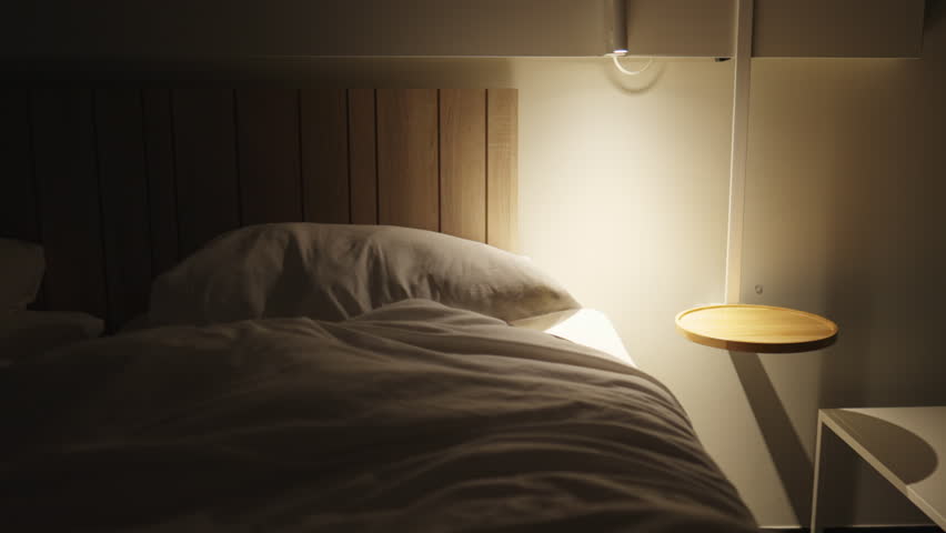 Young man laying in bed at night going to sleep. Male person lays under bedsheets and turning bedside night light off Royalty-Free Stock Footage #1100343567