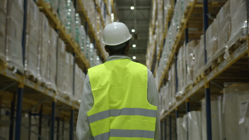 African American stocker walks among orders and products on racks in storehouse