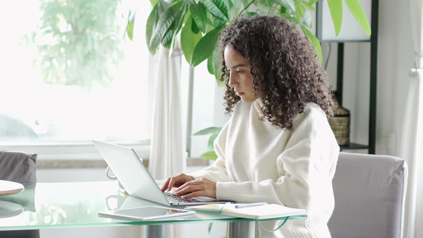 Young smiling latin woman student using laptop technology, checking email, browsing websites, remote working online or elearning from homeoffice sitting at table typing on pc computer. | Shutterstock HD Video #1100349071